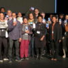 Participants on stage holding up their phones displaying personal images