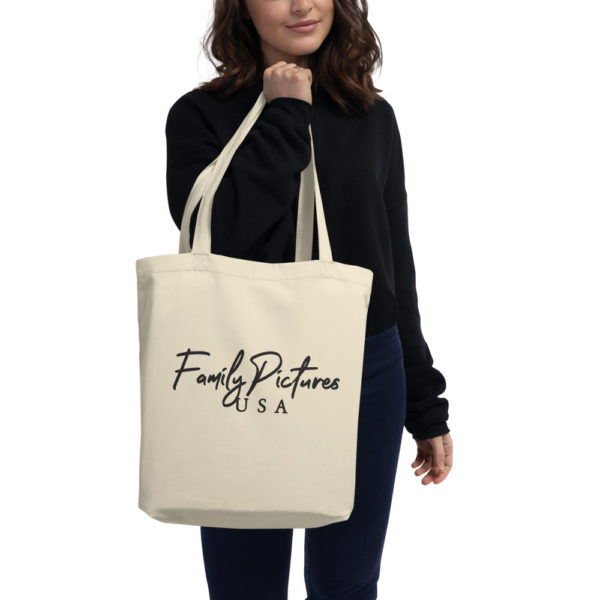 Model holds cream color tote with Family Pictures USA logo in black text.